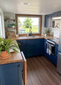 a kitchen with blue cabinets and wood floors, an oven, sink, dishwasher and window