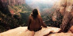 a woman sitting on top of a cliff looking down at the canyons and mountains