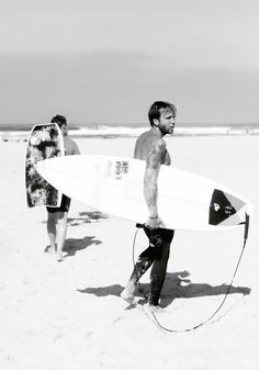 a man holding a surfboard on top of a sandy beach