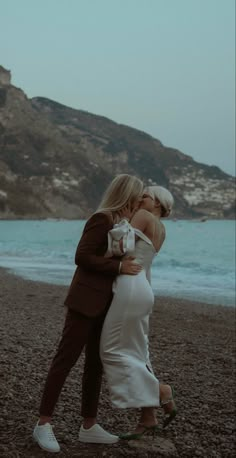 a man and woman kissing on the beach with mountains in the background at night time