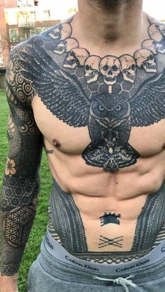 a man with an owl tattoo on his chest is standing in front of the grass