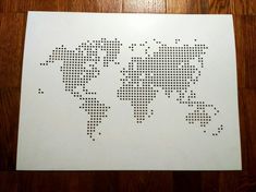 the world map is made out of small black dots on white paper, and sits on a wooden floor