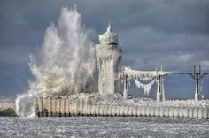 an ice covered lighthouse on the shore with waves crashing over it