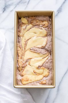 a loaf of bread with icing in a pan on a marble counter top next to a white towel