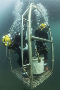 two divers in the water near a metal structure with ropes and buckets on it