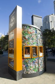 a building made out of cans and bottles in the middle of a street with buildings in the background