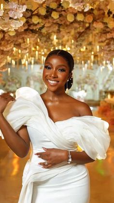 a woman in a white dress standing under a flower covered ceiling with lights and chandeliers