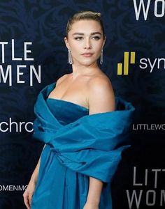 a woman in a blue dress standing on a red carpet with her hands behind her back