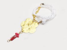 a white bracelet with a gold flower and red bead on the end is shown