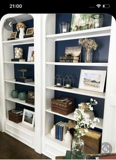 two white bookshelves with blue walls and flowers in vases on the table