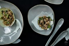 two white plates topped with food next to silver spoons and utensils on a black table