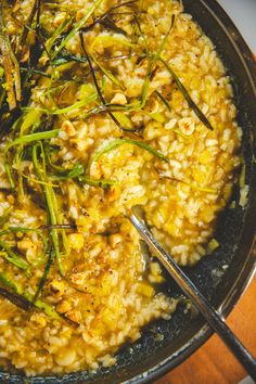 a bowl filled with rice and green onions on top of a wooden table next to a fork