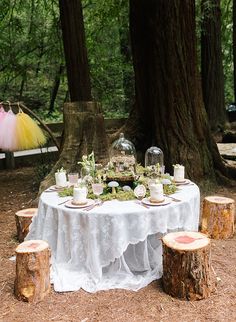 the table is set up in the woods for an outdoor dinner party with cake and candles