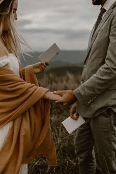 a man and woman standing next to each other in a field holding hands with one another