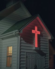 a red cross on the side of a white church at night with light from windows