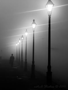 a person walking down a street in the fog at night with two lamps on either side