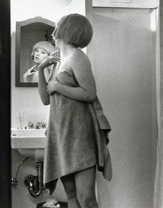 a woman standing in front of a bathroom mirror brushing her teeth and looking at herself in the mirror