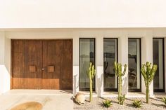 a white house with two brown doors and cactus plants in front of the door area