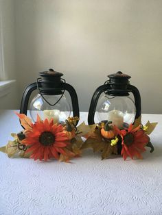 two glass vases with sunflowers and leaves in them on a white table