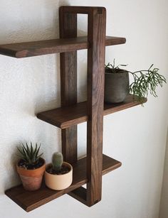 three wooden shelves with plants on them against a white wall and one shelf holding two potted plants