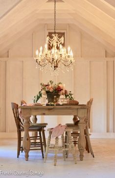 a chandelier hangs from the ceiling above a table with chairs and flowers on it