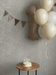 a cake sitting on top of a wooden table next to balloons and a balloon wall