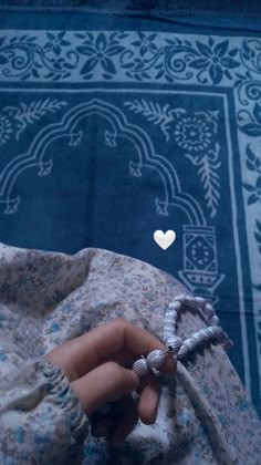 a hand holding a ring with a white heart on it and a rug in the background