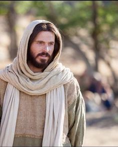 a man with long hair and a beard wearing a brown robe is standing in the woods