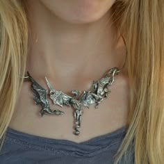 "Three magnificent dragons take flight in this stunning piece of sterling silver fantasy jewelry. The concept of the dragon necklace features three dimensional sculptures and an unique front clasp subtly incorporated into the design of the neckpiece; the result is a dragon trio statement necklace that seem to float around the wearer's neck, an artisan's creation that is sure to draw the eye of all who see it. Each of the dragons has a unique personality; the central dragon is the leader of the g Dragon Jewelry Clay, Unique Dragon Design Jewelry Pendant, Unique Dragon Design Pendant Jewelry, Silver Dragon Design Jewelry For Fantasy Events, Silver Fantasy Jewelry With Dragon Design, Fantasy Silver Jewelry With Dragon Design, Fantasy Style Silver Jewelry With Unique Design, Silver Necklace For Fantasy Events, Unique Metal Jewelry For Fantasy Events