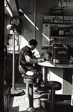 a man sitting at a table in front of a coffee shop writing on a piece of paper