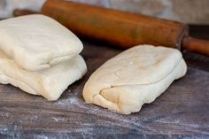 two uncooked doughs sitting on top of a wooden table next to a rolling pin