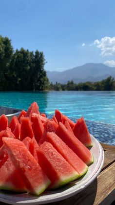 slices of watermelon are on a white plate near the edge of a pool