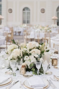 the table is set with white flowers and gold place settings for an elegant wedding reception