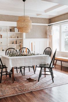 a dining room table with chairs and a white table cloth on it, in front of a window