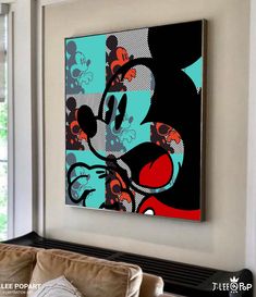 a mickey mouse painting hanging on the wall in a living room with couches and windows