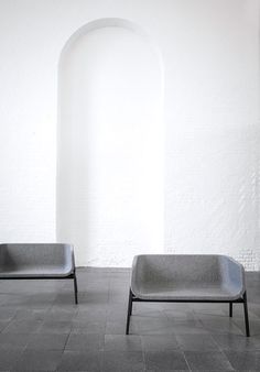 two gray chairs sitting next to each other on a tile floor in front of a white wall