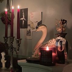 candles are lit on a table in front of a swan statue and other items that include figurines