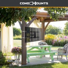 a green picnic table sitting under a pergolated covered gazebo with flowers in the background