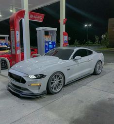 a white mustang parked in front of a gas station