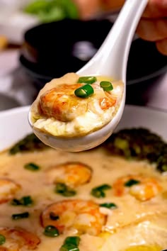 a spoon full of shrimp and grits with broccoli on it is being held over a bowl