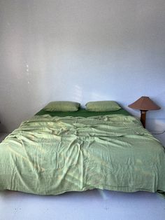 a bed with green sheets and pillows in a white room next to a lamp on the floor