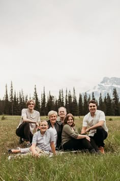 a group of people sitting on top of a grass covered field in front of trees