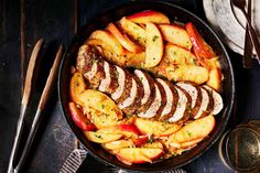 a pan filled with meat and vegetables on top of a wooden table next to utensils