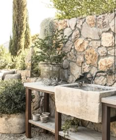 an outdoor garden with stone walls and potted plants on the table, surrounded by trees