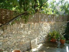 a stone wall with potted plants on the side and trees in the back ground