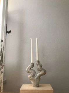 two white candles sitting on top of a wooden block