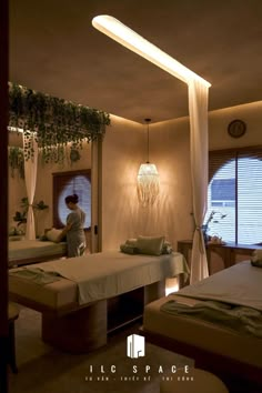 a woman is standing in the middle of a room with two beds and plants hanging from the ceiling