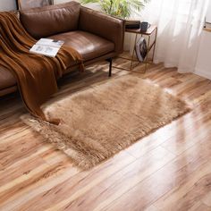 a living room with wooden floors and a brown couch in the corner, next to a window