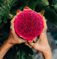 two hands holding up a piece of fruit in front of some green plants and leaves