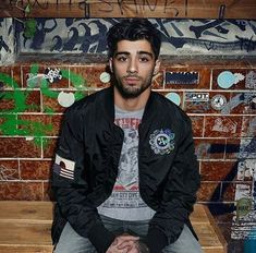 a man sitting on top of a wooden bench in front of a wall covered with graffiti